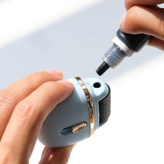 Hand holding a small stamp with an ink bottle component against a light background